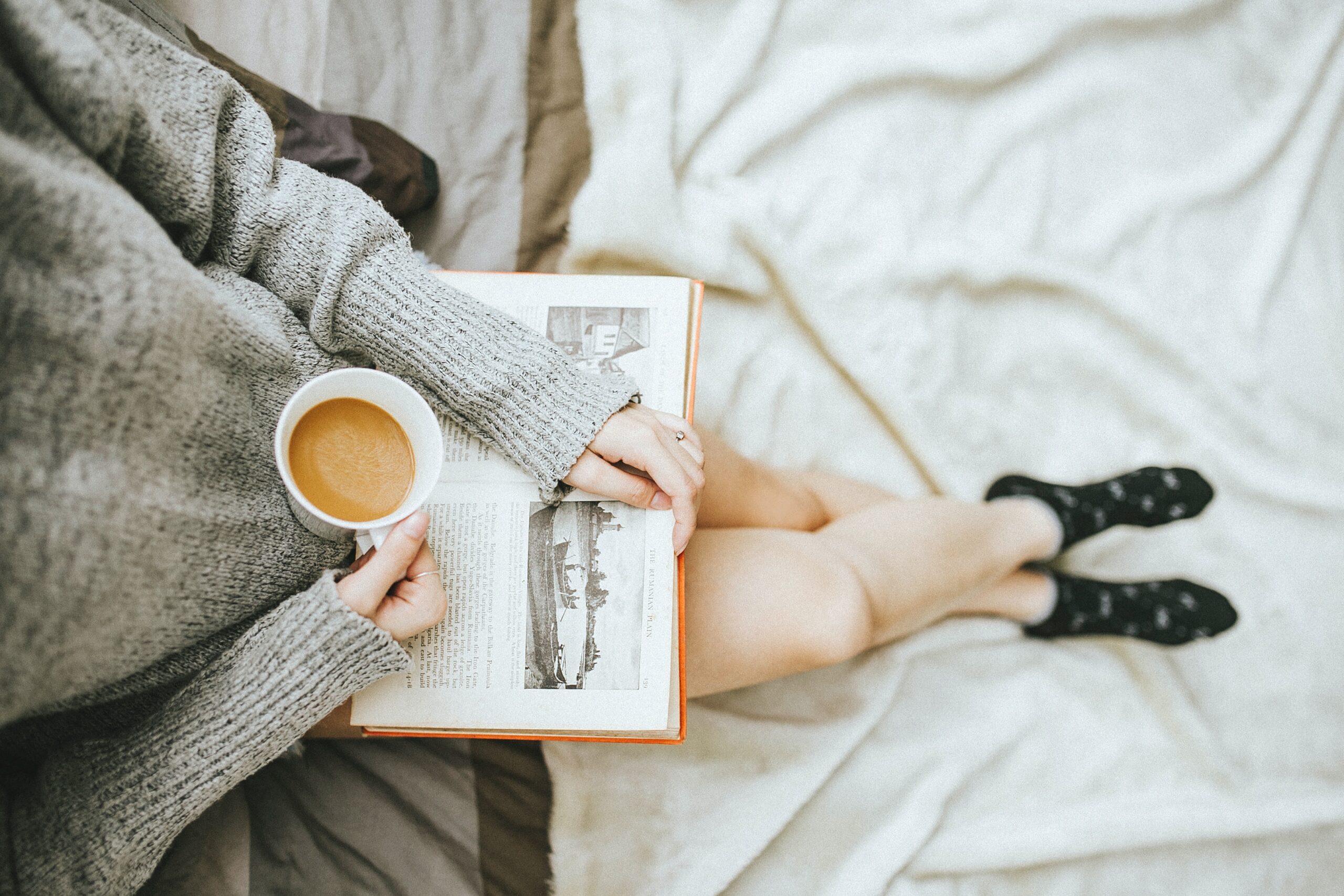 Person holding an open book in their lap and holding a full coffee cup