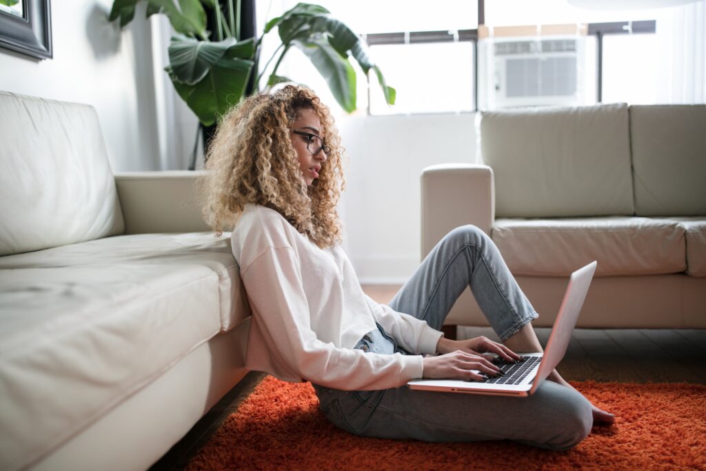 Woman sitting on the floor reading wellness websites from a laptop on her lap