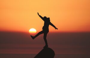 Person balancing on one leg on top of a boulder with a sunset in the background